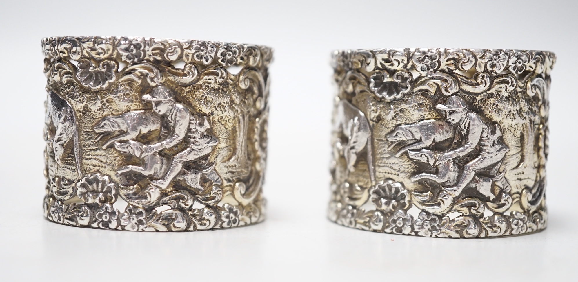 A pair of Edwardian silver serviette rings, pierced and embossed with deer hunting scenes, Wakely & Wheeler, London, 1906, 38mm.